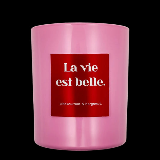 Pink candle with a red label displaying 'La vie est belle' on a black background