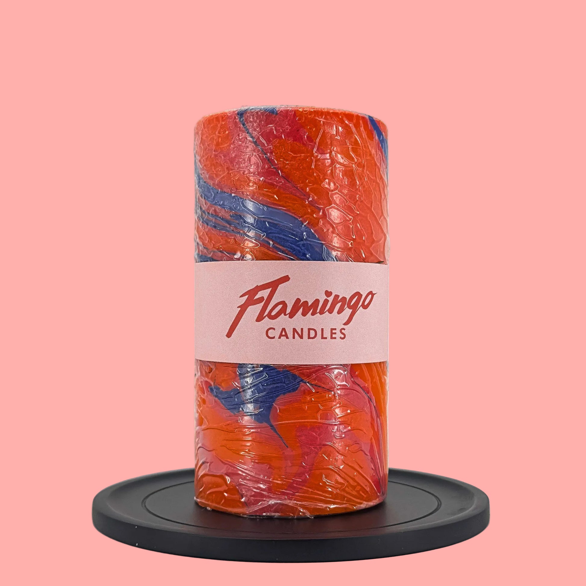 Cylindrical candle with orange and blue marbled design on a white background, featuring 'Flamingo Candles' branding.